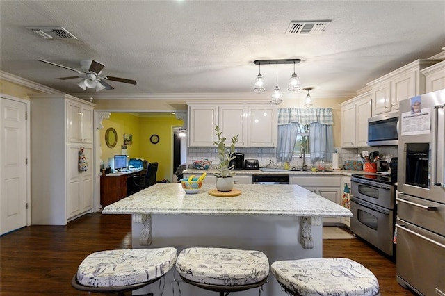 kitchen featuring appliances with stainless steel finishes, crown molding, dark hardwood / wood-style floors, a kitchen island, and hanging light fixtures