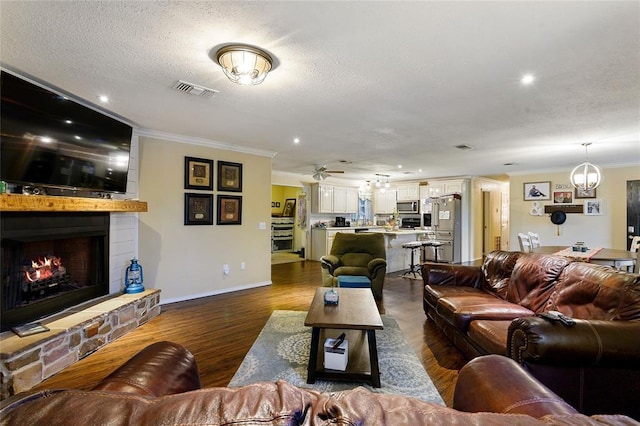 living room with dark hardwood / wood-style floors, a stone fireplace, ornamental molding, and a textured ceiling