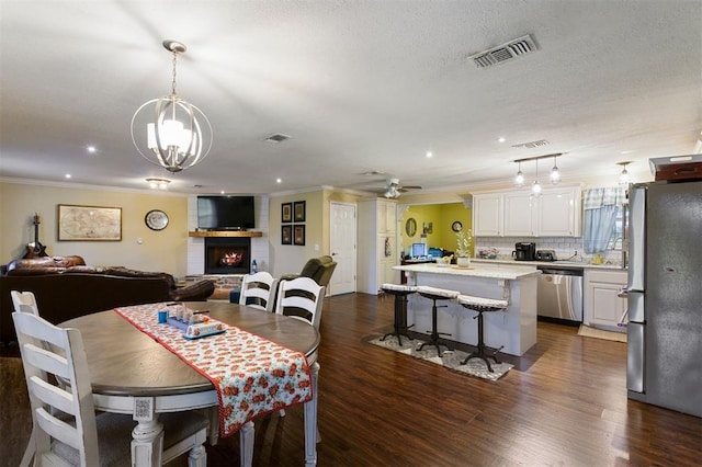 dining space featuring ceiling fan with notable chandelier, a large fireplace, crown molding, and dark wood-type flooring