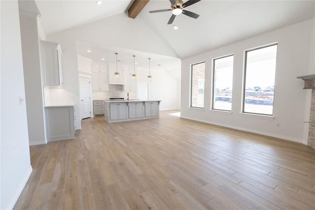 unfurnished living room with vaulted ceiling with beams, ceiling fan, sink, and light wood-type flooring