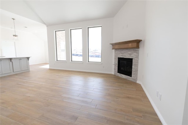 unfurnished living room featuring lofted ceiling, a fireplace, and light hardwood / wood-style flooring