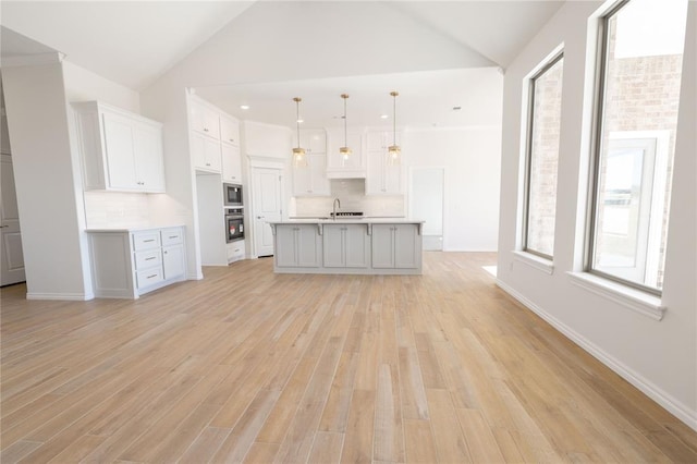 kitchen with hanging light fixtures, backsplash, an island with sink, and appliances with stainless steel finishes