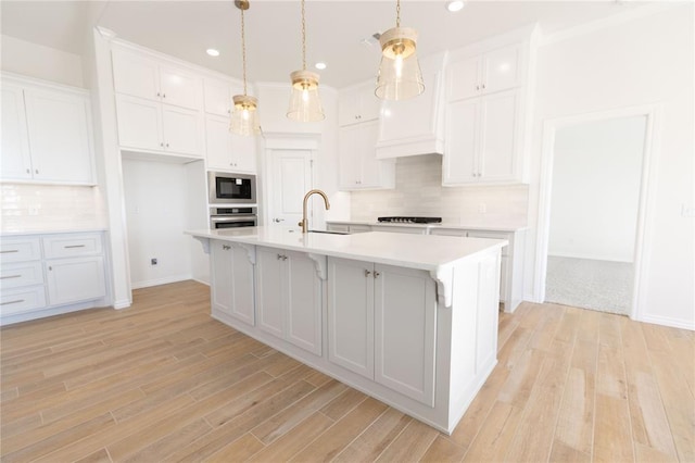 kitchen featuring sink, black appliances, white cabinets, a center island with sink, and decorative light fixtures