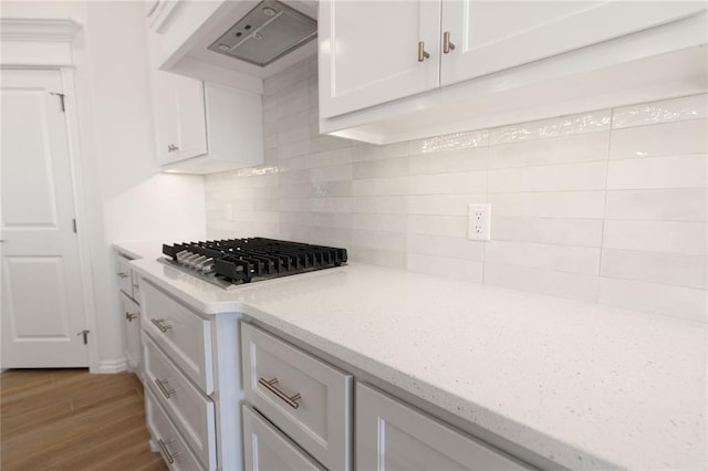 kitchen featuring white cabinetry, wood-type flooring, backsplash, stainless steel gas cooktop, and light stone counters