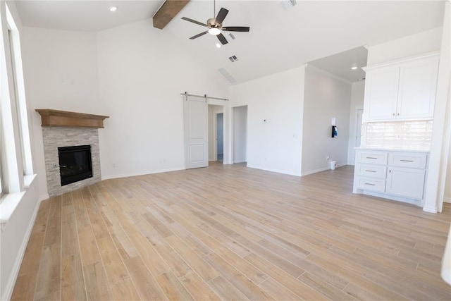 unfurnished living room featuring a fireplace, ceiling fan, a barn door, beam ceiling, and light hardwood / wood-style flooring