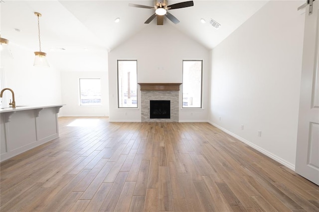 unfurnished living room featuring sink, vaulted ceiling, a tile fireplace, ceiling fan, and light hardwood / wood-style floors