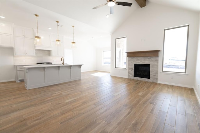 unfurnished living room featuring beamed ceiling, ceiling fan, sink, and light hardwood / wood-style floors