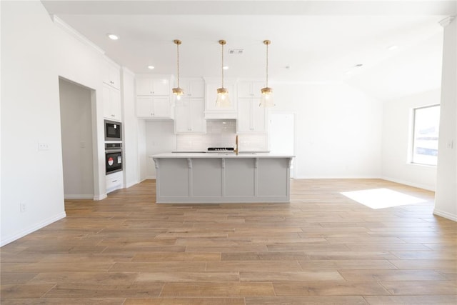 kitchen with vaulted ceiling, built in microwave, oven, hanging light fixtures, and a kitchen island with sink