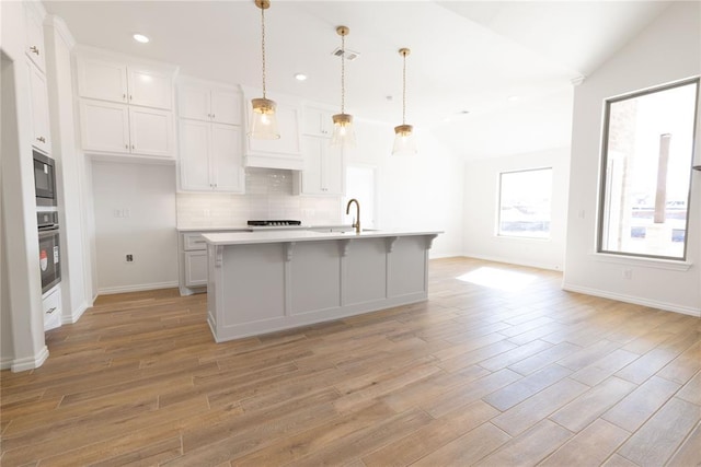 kitchen with lofted ceiling, black microwave, oven, and a center island with sink