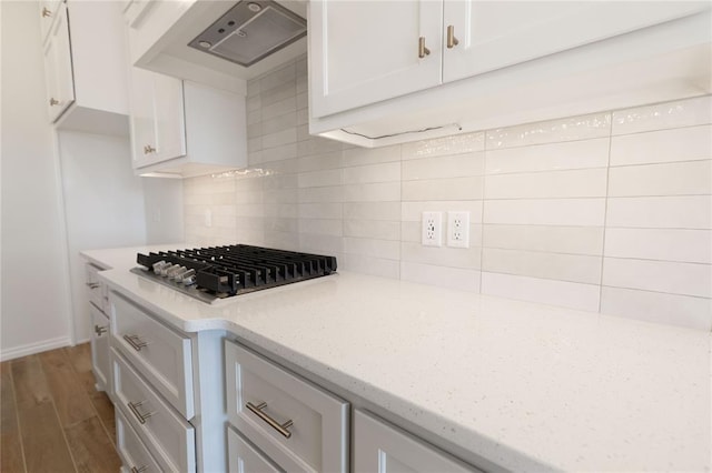 kitchen with hardwood / wood-style floors, stainless steel gas stovetop, white cabinetry, backsplash, and wall chimney exhaust hood