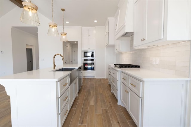 kitchen featuring premium range hood, appliances with stainless steel finishes, white cabinetry, sink, and a kitchen island with sink