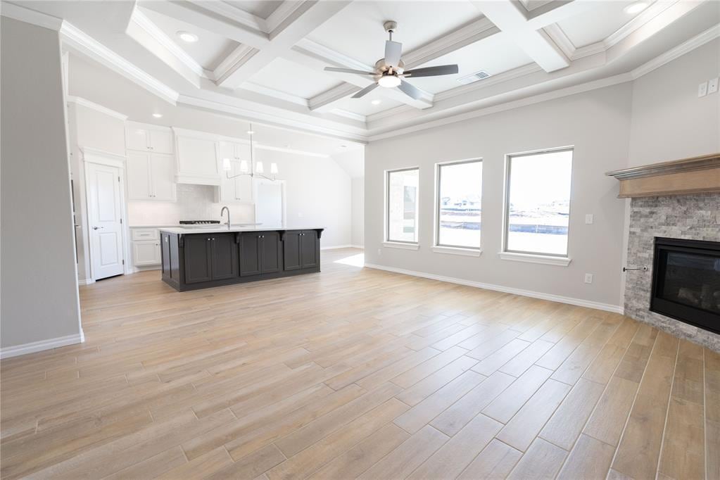 unfurnished living room with coffered ceiling, ceiling fan with notable chandelier, a fireplace, and ornamental molding