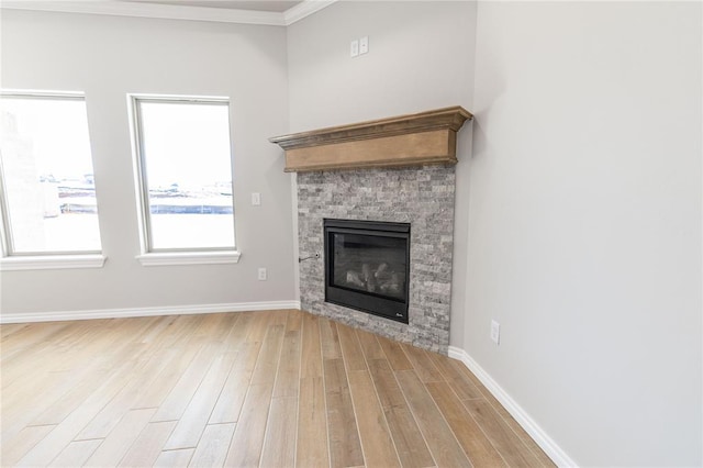 unfurnished living room with ornamental molding, a stone fireplace, and light hardwood / wood-style flooring