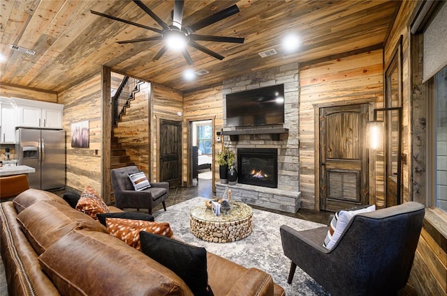 living room featuring a stone fireplace, ceiling fan, wooden ceiling, and wood walls