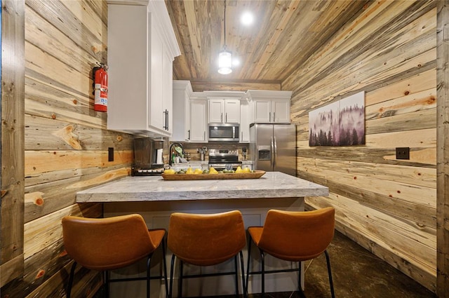 kitchen featuring stainless steel appliances, kitchen peninsula, wood walls, a breakfast bar area, and white cabinets