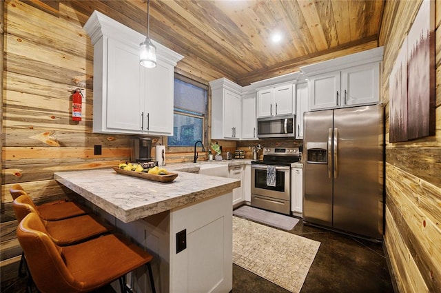 kitchen featuring a breakfast bar, white cabinets, hanging light fixtures, wooden walls, and appliances with stainless steel finishes