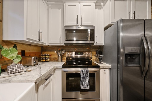 kitchen with white cabinets, appliances with stainless steel finishes, light stone countertops, and sink