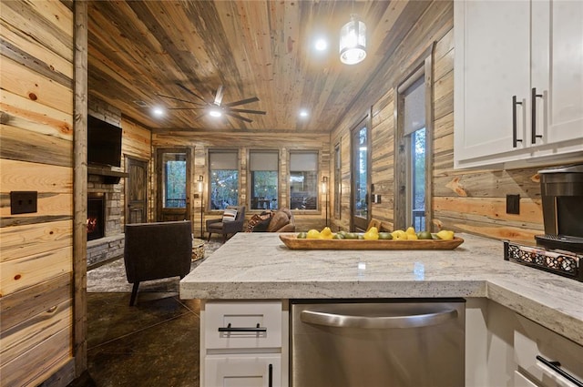 kitchen featuring white cabinets, dishwasher, wood walls, and a fireplace