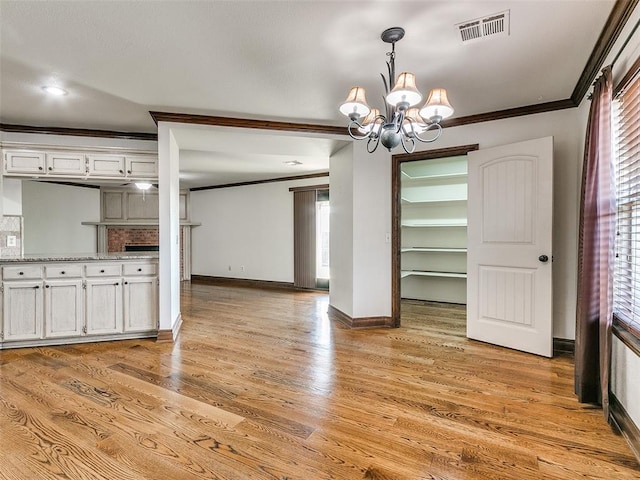 unfurnished dining area featuring light hardwood / wood-style floors, an inviting chandelier, ornamental molding, and a brick fireplace