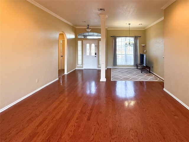 foyer entrance featuring dark wood-type flooring, ornamental molding, an inviting chandelier, and ornate columns