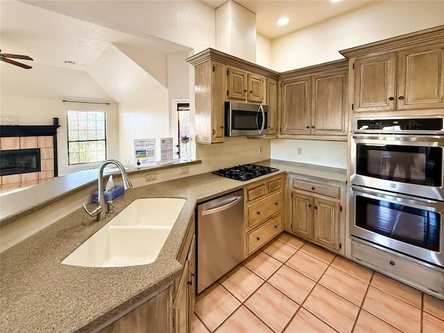 kitchen with light tile patterned flooring, sink, appliances with stainless steel finishes, a fireplace, and decorative backsplash