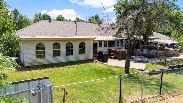 back of house featuring a hot tub, a patio area, and a lawn