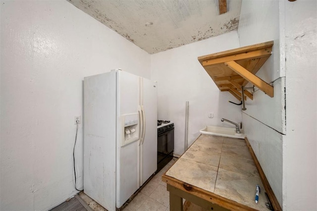 kitchen with tile countertops, black gas range, white fridge with ice dispenser, and sink