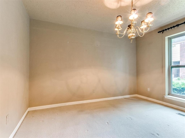 carpeted spare room featuring a textured ceiling and an inviting chandelier