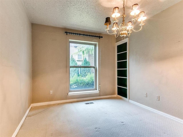 spare room with carpet flooring, a textured ceiling, and a notable chandelier