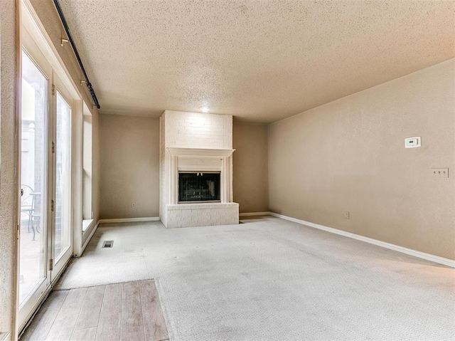 unfurnished living room featuring a textured ceiling, light carpet, and a brick fireplace