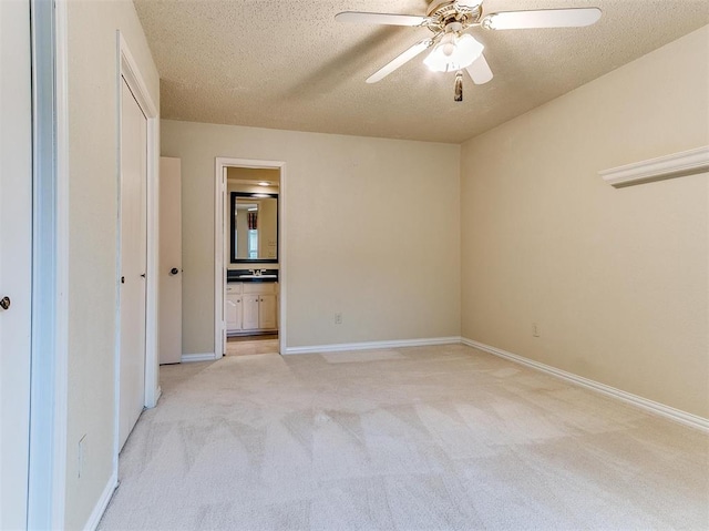 unfurnished bedroom with ceiling fan, light colored carpet, a textured ceiling, and ensuite bath