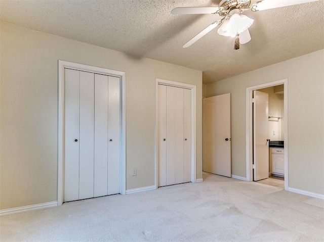 unfurnished bedroom featuring connected bathroom, ceiling fan, a textured ceiling, light carpet, and two closets