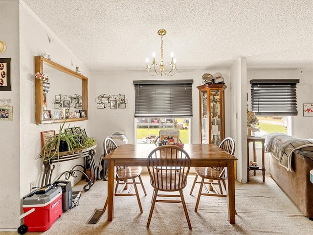 carpeted dining space with a healthy amount of sunlight, a textured ceiling, and a notable chandelier