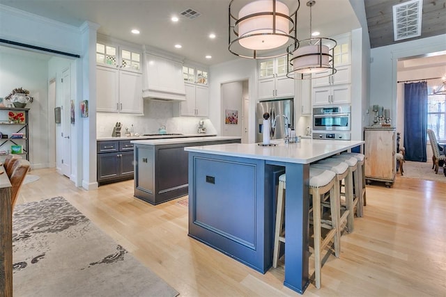 kitchen featuring an island with sink, light hardwood / wood-style floors, pendant lighting, white cabinets, and appliances with stainless steel finishes