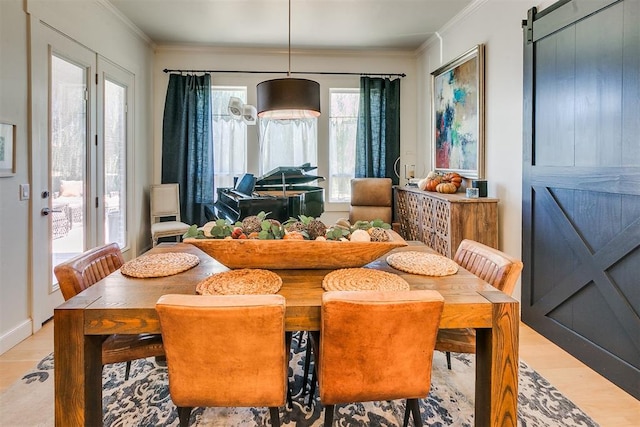 dining area featuring plenty of natural light, a barn door, light wood-type flooring, and ornamental molding