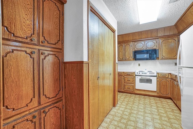 kitchen featuring a textured ceiling, white appliances, and wood walls