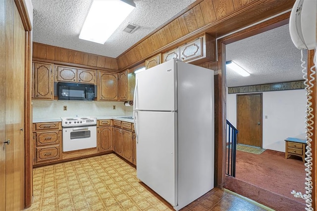 kitchen with a textured ceiling, wood walls, light colored carpet, and white appliances