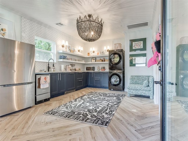 kitchen featuring stainless steel appliances, a notable chandelier, stacked washer / dryer, light parquet flooring, and ornamental molding