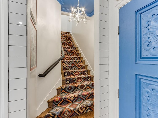 staircase featuring wood-type flooring, a chandelier, and ornamental molding