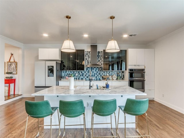 kitchen featuring white cabinets, a kitchen island with sink, and wall chimney exhaust hood