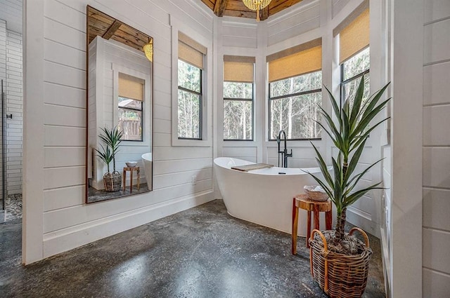 bathroom featuring a bathing tub, a notable chandelier, and concrete floors