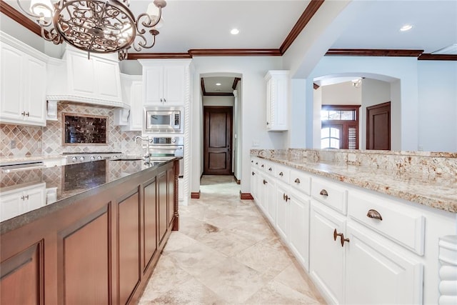 kitchen with pendant lighting, light stone countertops, ornamental molding, white cabinetry, and stainless steel appliances