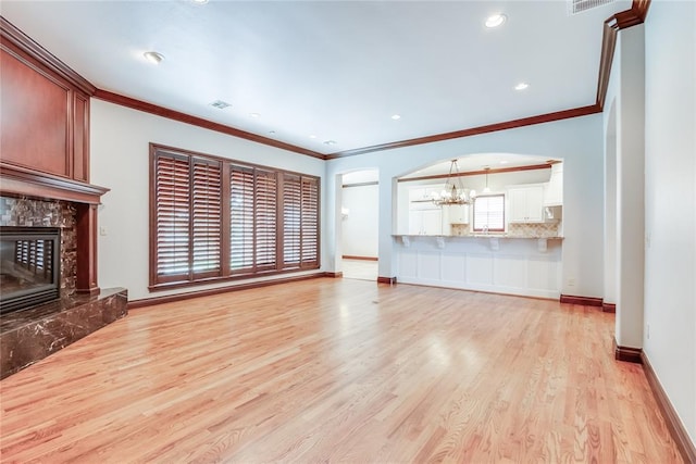 unfurnished living room featuring a fireplace, an inviting chandelier, light hardwood / wood-style flooring, and crown molding