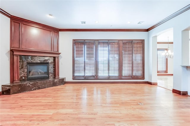 unfurnished living room with a notable chandelier, light wood-type flooring, crown molding, and a high end fireplace