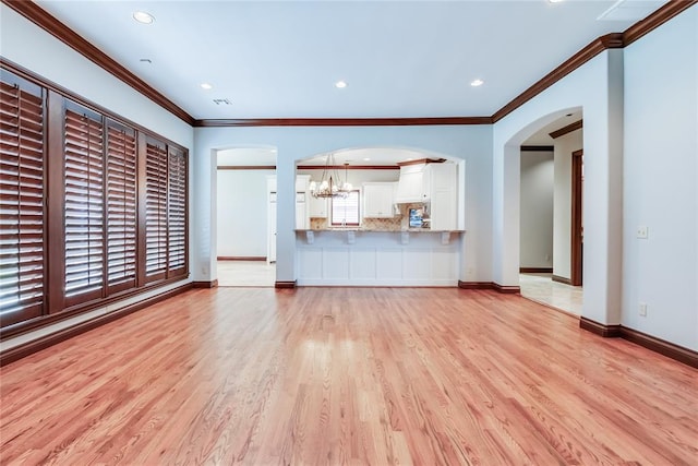 unfurnished living room with crown molding, light hardwood / wood-style flooring, and a chandelier