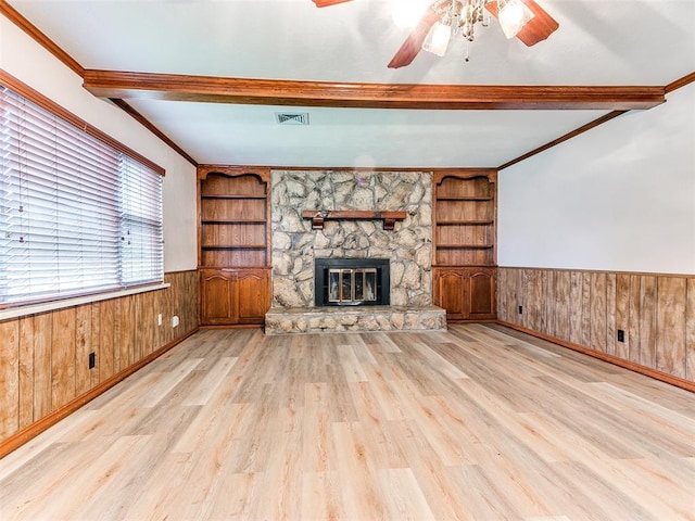 unfurnished living room featuring built in shelves, light hardwood / wood-style floors, a stone fireplace, and wooden walls