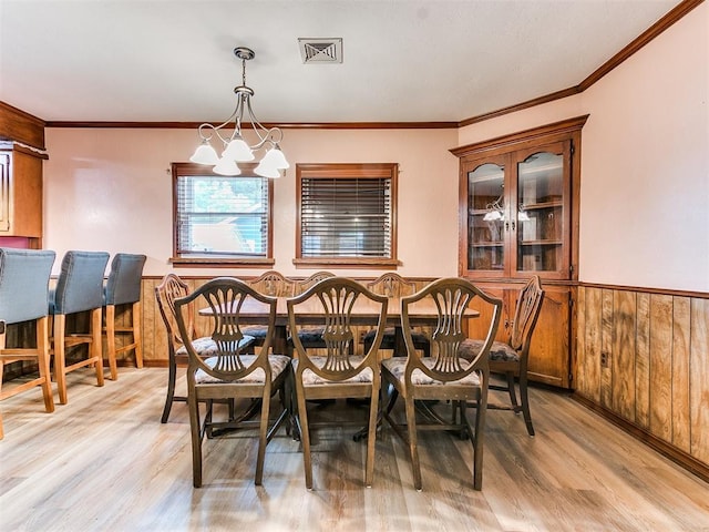 dining space featuring wood walls, an inviting chandelier, ornamental molding, and light wood-type flooring