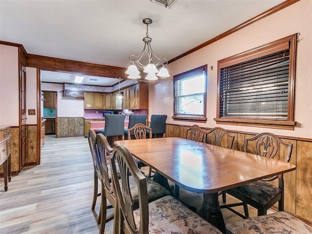 dining area featuring crown molding, light hardwood / wood-style flooring, wood walls, and an inviting chandelier