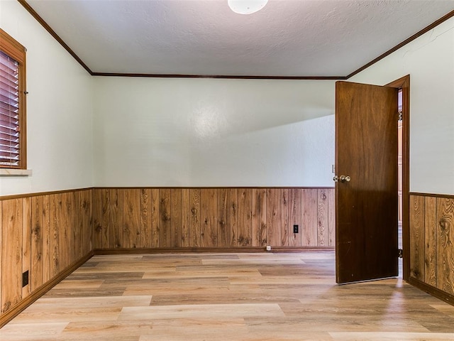 spare room with a textured ceiling, light hardwood / wood-style flooring, ornamental molding, and wood walls