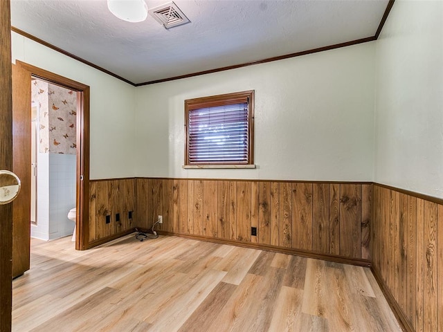 spare room featuring wood walls, light hardwood / wood-style floors, a textured ceiling, and ornamental molding